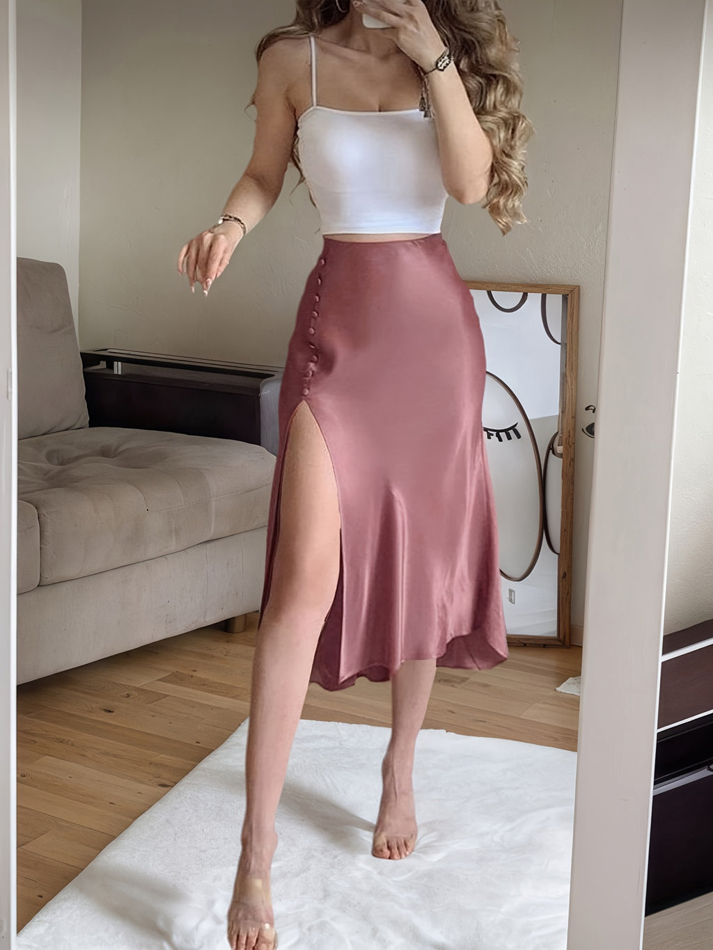 Woman wearing a white top and pink satin skirt in a room with a couch and mirror.