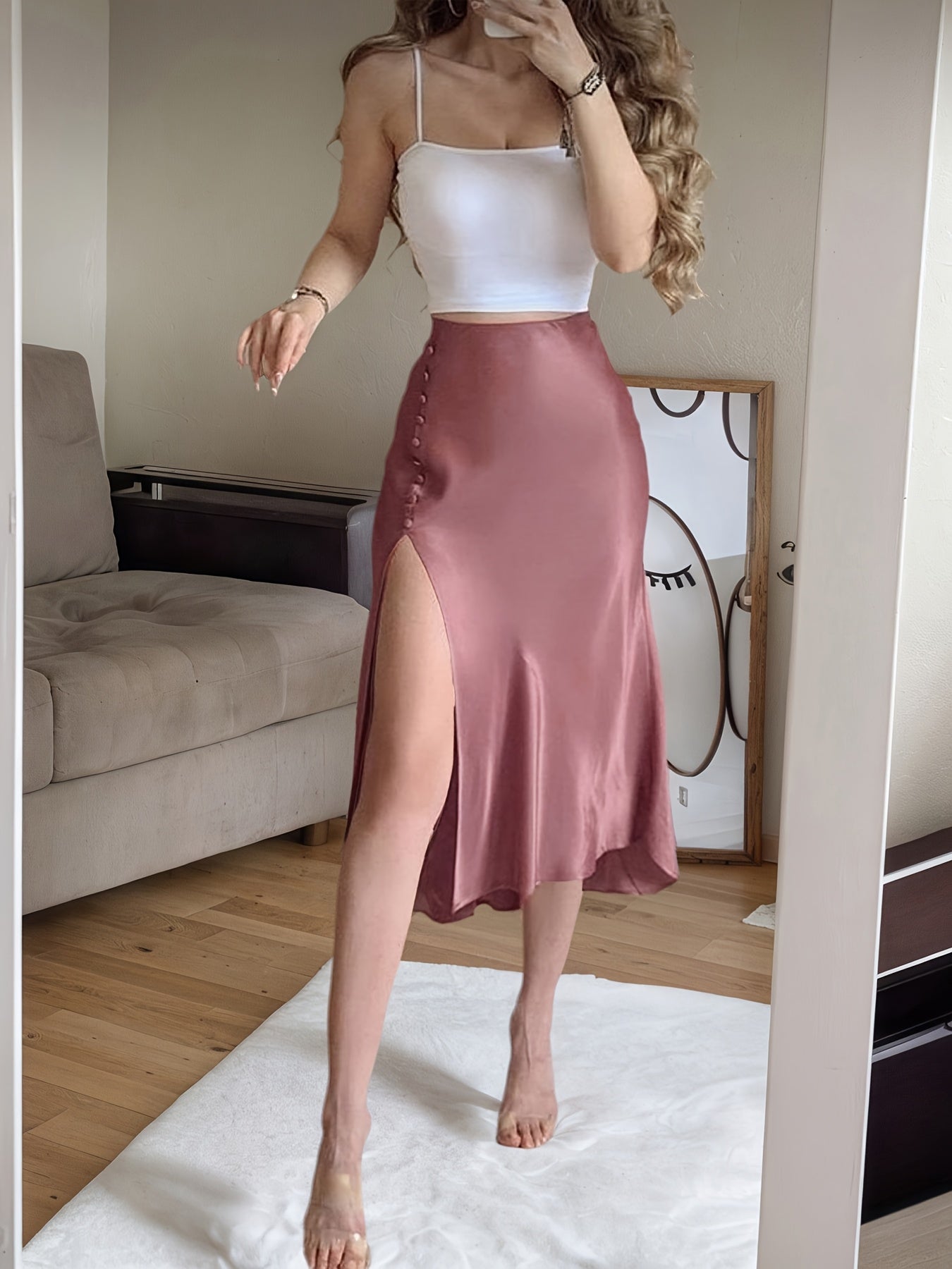 Woman wearing a white top and pink satin skirt in a room with a couch and mirror.