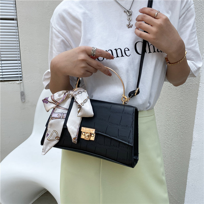 Person holding a black handbag with a decorative ribbon, wearing a white shirt and light green pants.