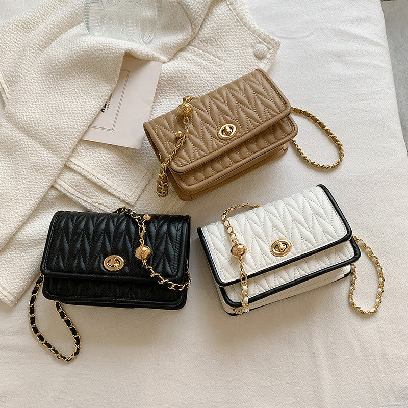 Three quilted handbags in beige, black, and white with gold chains on a textured surface.